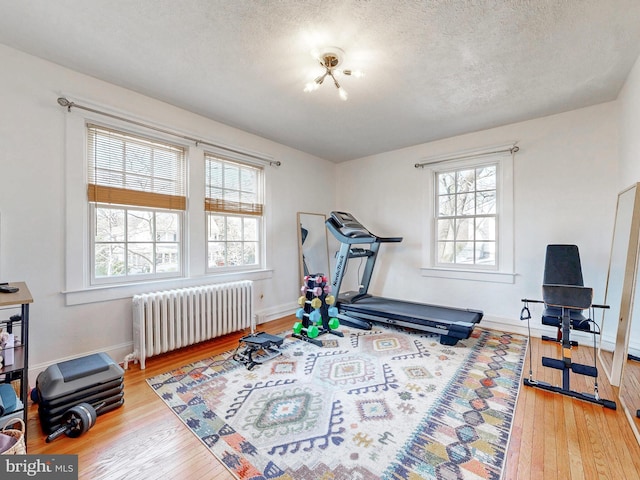 exercise room with hardwood / wood-style floors, a wealth of natural light, radiator heating unit, and a textured ceiling