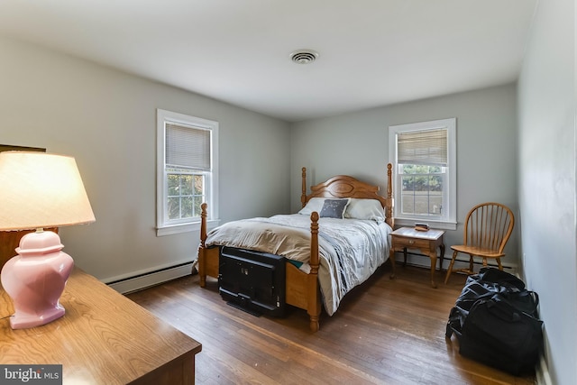 bedroom with multiple windows, a baseboard heating unit, and dark wood-type flooring