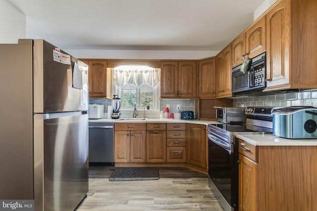 kitchen with stainless steel appliances, sink, backsplash, and light hardwood / wood-style flooring