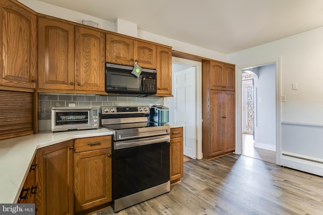 kitchen with stainless steel electric range oven, a baseboard heating unit, decorative backsplash, and light wood-type flooring