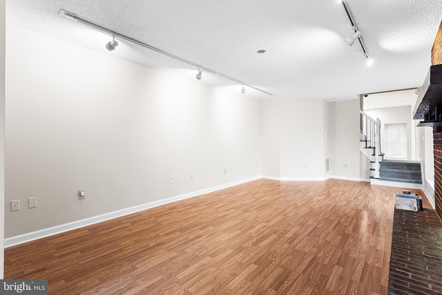 unfurnished living room featuring hardwood / wood-style flooring, rail lighting, and a textured ceiling