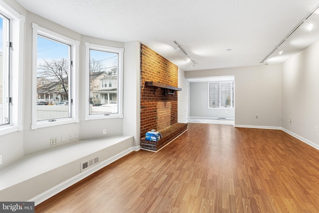 unfurnished living room with track lighting, a textured ceiling, light hardwood / wood-style floors, and a fireplace