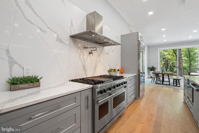 kitchen with gray cabinetry, double oven range, light stone countertops, and island exhaust hood