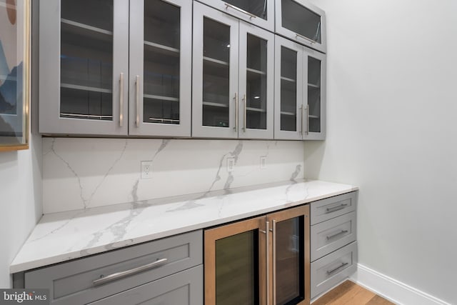 bar featuring gray cabinets, beverage cooler, light stone counters, and light hardwood / wood-style floors