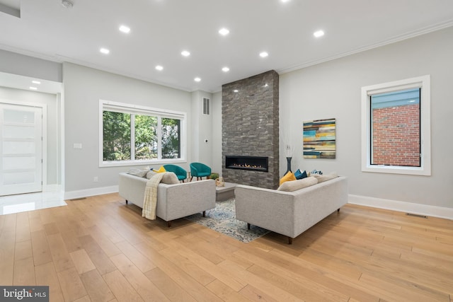 living room featuring crown molding, a stone fireplace, and light hardwood / wood-style flooring