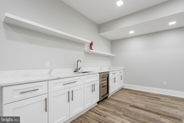 kitchen featuring sink, light hardwood / wood-style flooring, white cabinetry, wine cooler, and light stone counters