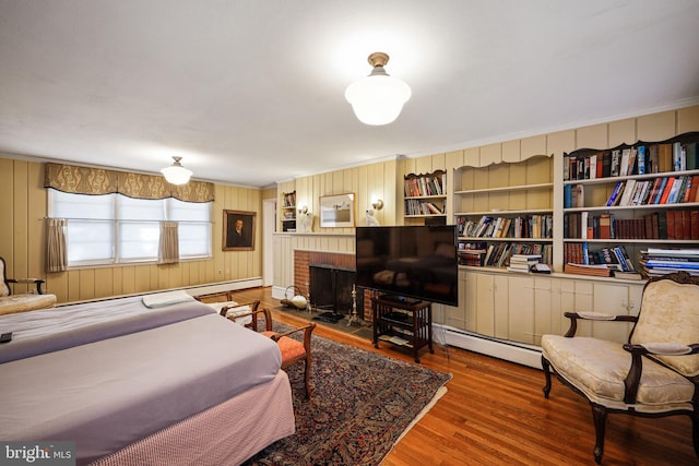 bedroom with a brick fireplace, wood-type flooring, and baseboard heating