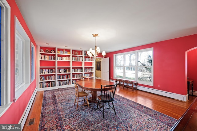 dining area featuring hardwood / wood-style flooring, a baseboard radiator, and a chandelier