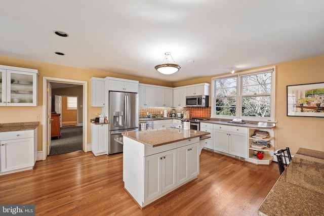 kitchen featuring white cabinetry, light stone counters, light wood-type flooring, appliances with stainless steel finishes, and a kitchen island