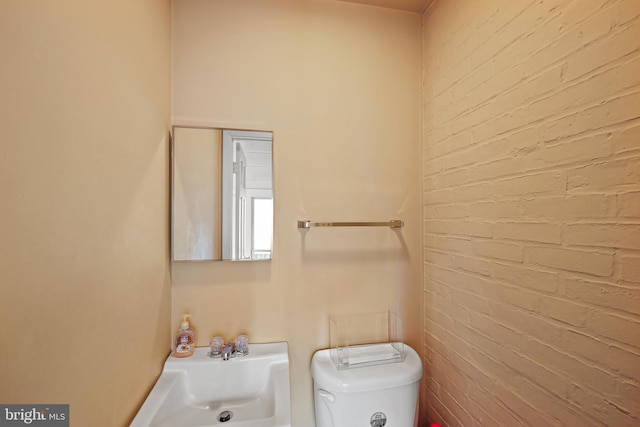 bathroom featuring brick wall, sink, and toilet