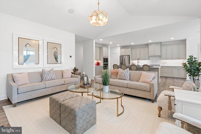 living room featuring light wood-type flooring, high vaulted ceiling, sink, and a notable chandelier