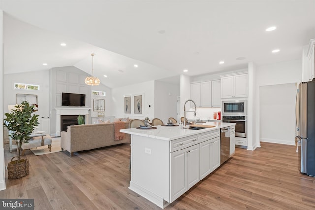 kitchen with sink, stainless steel appliances, light stone counters, white cabinets, and a center island with sink