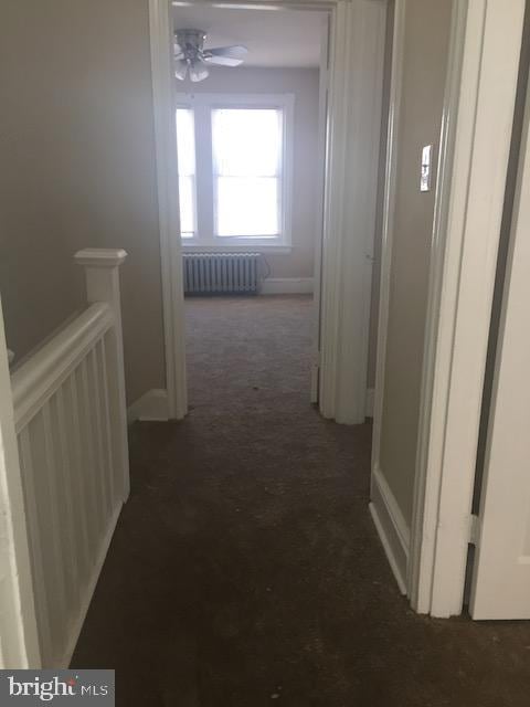 hall with radiator heating unit and dark colored carpet