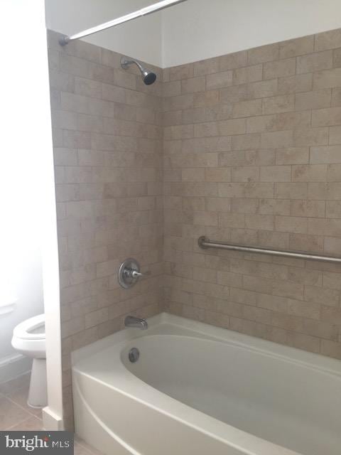 bathroom featuring tiled shower / bath, tile patterned floors, and toilet