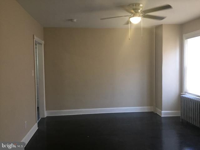 empty room featuring dark wood-type flooring, radiator heating unit, and ceiling fan