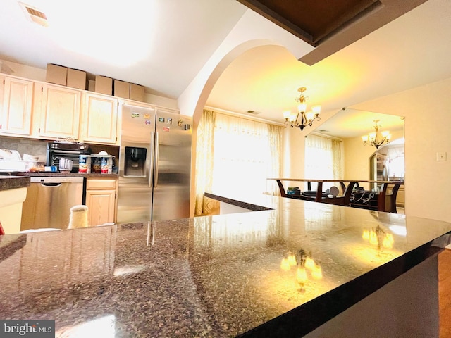 kitchen featuring pendant lighting, stainless steel appliances, tasteful backsplash, dark stone countertops, and a chandelier