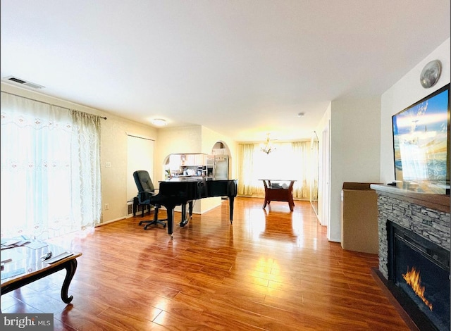 living area featuring an inviting chandelier, a fireplace, visible vents, and wood finished floors