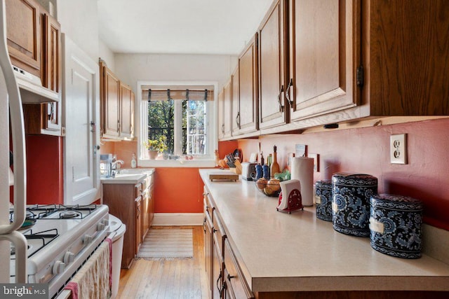 kitchen with sink, gas range gas stove, and light wood-type flooring