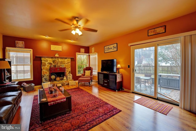 living room with ceiling fan, a stone fireplace, and light hardwood / wood-style floors