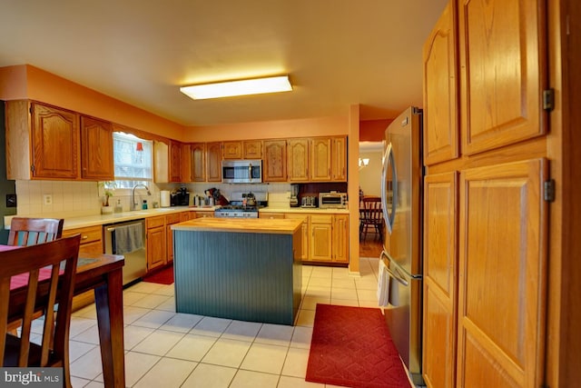 kitchen featuring sink, light tile patterned floors, backsplash, stainless steel appliances, and a center island