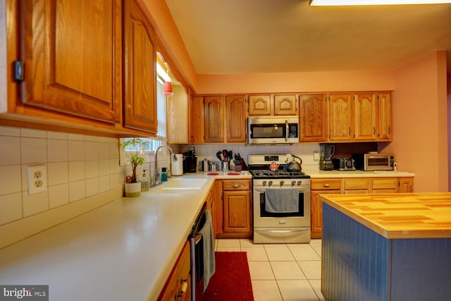 kitchen featuring sink, light tile patterned floors, appliances with stainless steel finishes, butcher block counters, and backsplash