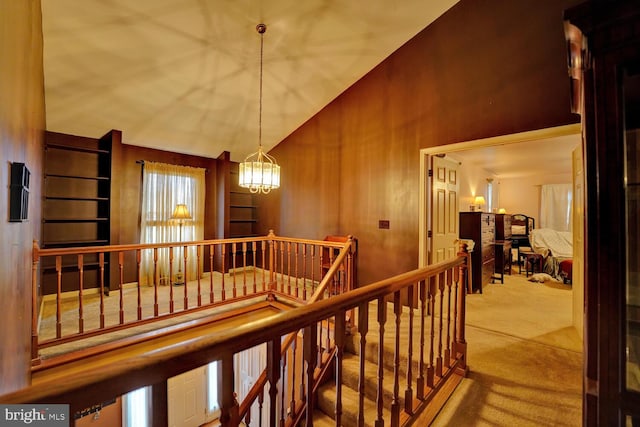 hallway featuring carpet floors, high vaulted ceiling, wooden walls, and a chandelier