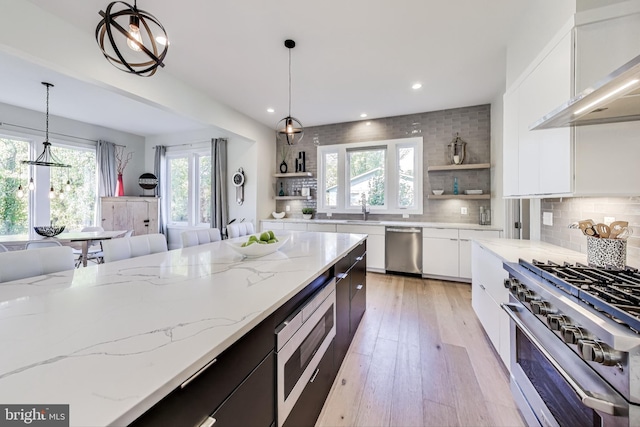 kitchen with pendant lighting, sink, white cabinets, stainless steel appliances, and light stone countertops