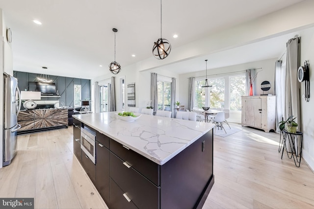 kitchen with appliances with stainless steel finishes, decorative light fixtures, light wood-type flooring, and a spacious island