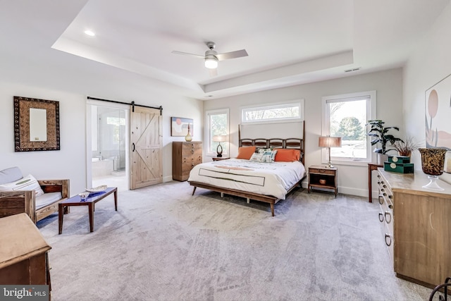 bedroom with a barn door, light colored carpet, ensuite bathroom, and a tray ceiling