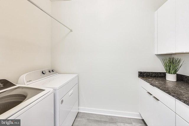 clothes washing area with washer and clothes dryer, light hardwood / wood-style floors, and cabinets