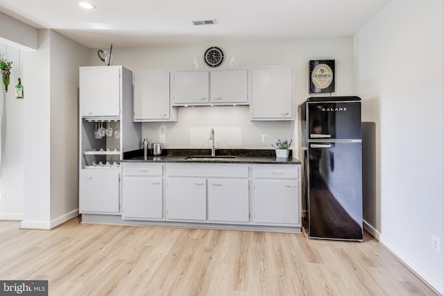 kitchen featuring white cabinetry, sink, light hardwood / wood-style floors, and black fridge