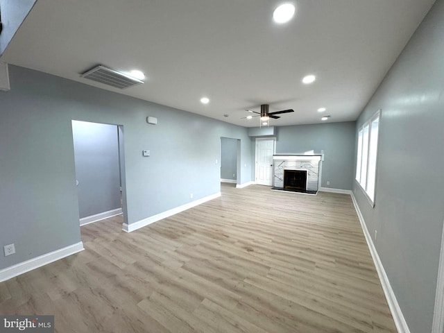 unfurnished living room featuring a premium fireplace, ceiling fan, and light hardwood / wood-style floors