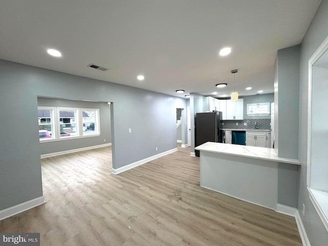 kitchen featuring stainless steel refrigerator, kitchen peninsula, dishwasher, pendant lighting, and white cabinets