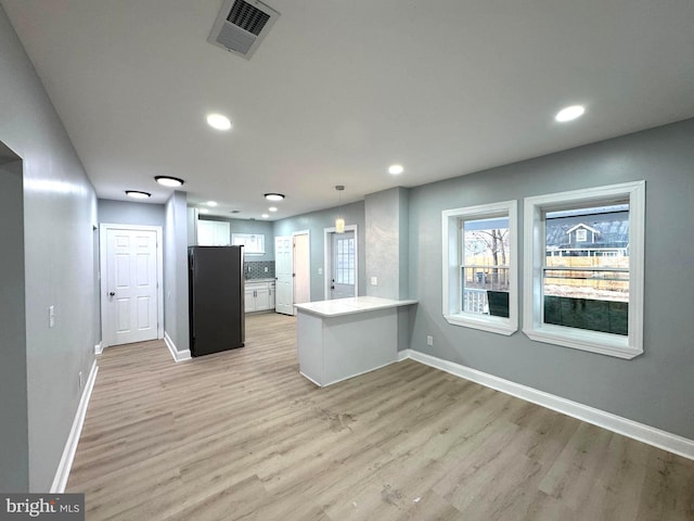 kitchen with white cabinetry, stainless steel fridge, hanging light fixtures, kitchen peninsula, and light wood-type flooring