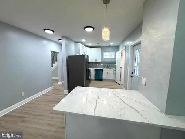 kitchen with pendant lighting, white cabinetry, backsplash, light hardwood / wood-style floors, and stainless steel appliances