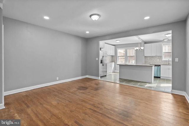 unfurnished living room featuring an inviting chandelier, sink, and light hardwood / wood-style flooring