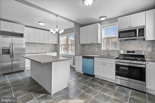 kitchen with pendant lighting, sink, stainless steel appliances, white cabinets, and a kitchen island