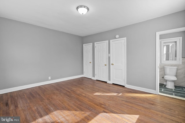 unfurnished bedroom featuring connected bathroom, two closets, and dark hardwood / wood-style flooring