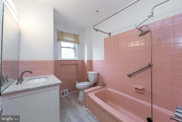 full bathroom with toilet, tiled shower / bath, wood-type flooring, tile walls, and vanity