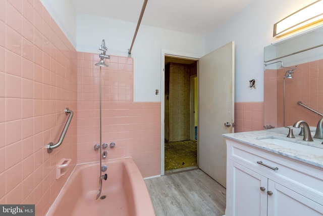 bathroom with hardwood / wood-style floors, vanity, tiled shower / bath combo, and tile walls