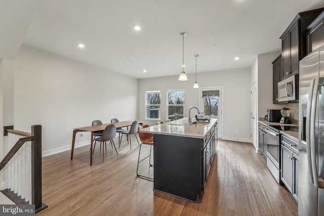 kitchen featuring sink, stainless steel appliances, wood-type flooring, an island with sink, and decorative light fixtures