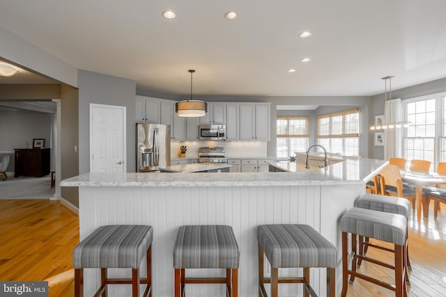 kitchen with a large island, appliances with stainless steel finishes, tasteful backsplash, light hardwood / wood-style floors, and decorative light fixtures