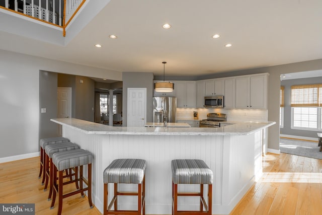 kitchen featuring light stone counters, a kitchen breakfast bar, pendant lighting, stainless steel appliances, and white cabinets