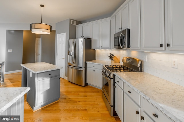 kitchen featuring a kitchen island, appliances with stainless steel finishes, decorative light fixtures, light stone countertops, and light wood-type flooring