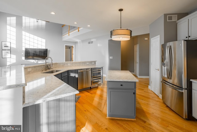 kitchen with sink, gray cabinetry, appliances with stainless steel finishes, a kitchen island, and beverage cooler