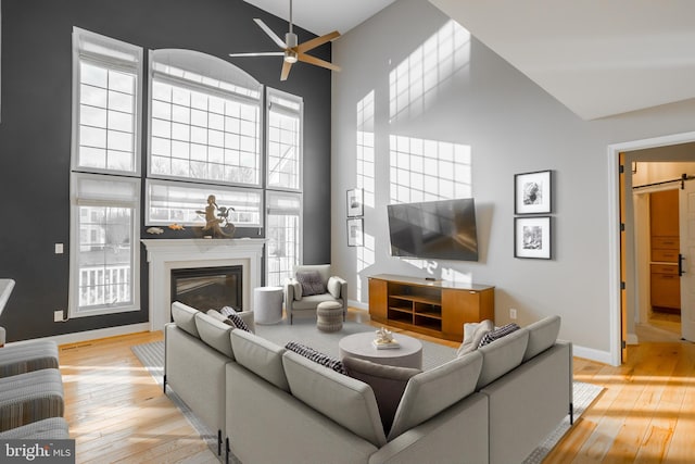 living room with a premium fireplace, a barn door, high vaulted ceiling, and light wood-type flooring