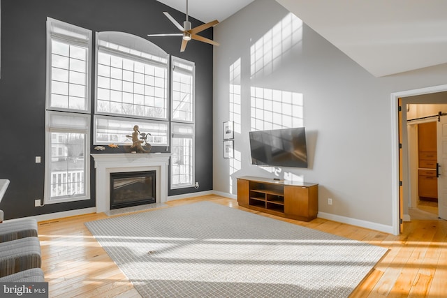 living room featuring high vaulted ceiling, wood-type flooring, ceiling fan, a high end fireplace, and a barn door