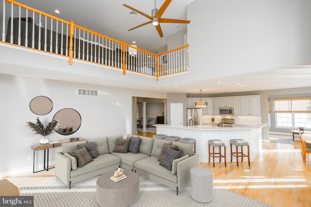 living room featuring a high ceiling, ceiling fan, and light wood-type flooring