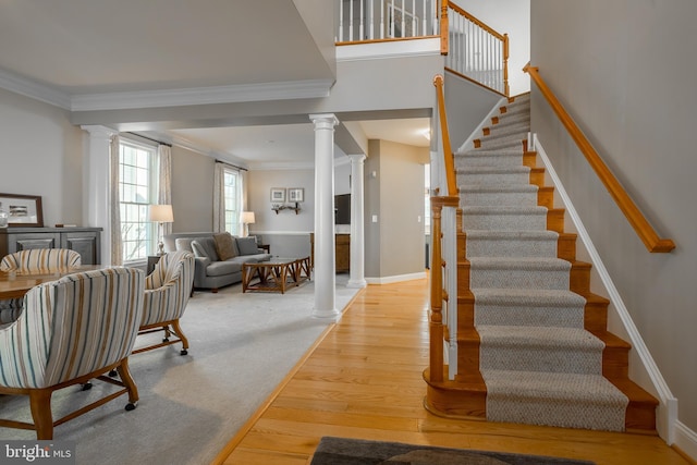 stairway featuring hardwood / wood-style floors, crown molding, and decorative columns