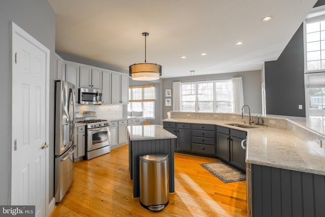 kitchen with sink, gray cabinets, hanging light fixtures, stainless steel appliances, and a kitchen island